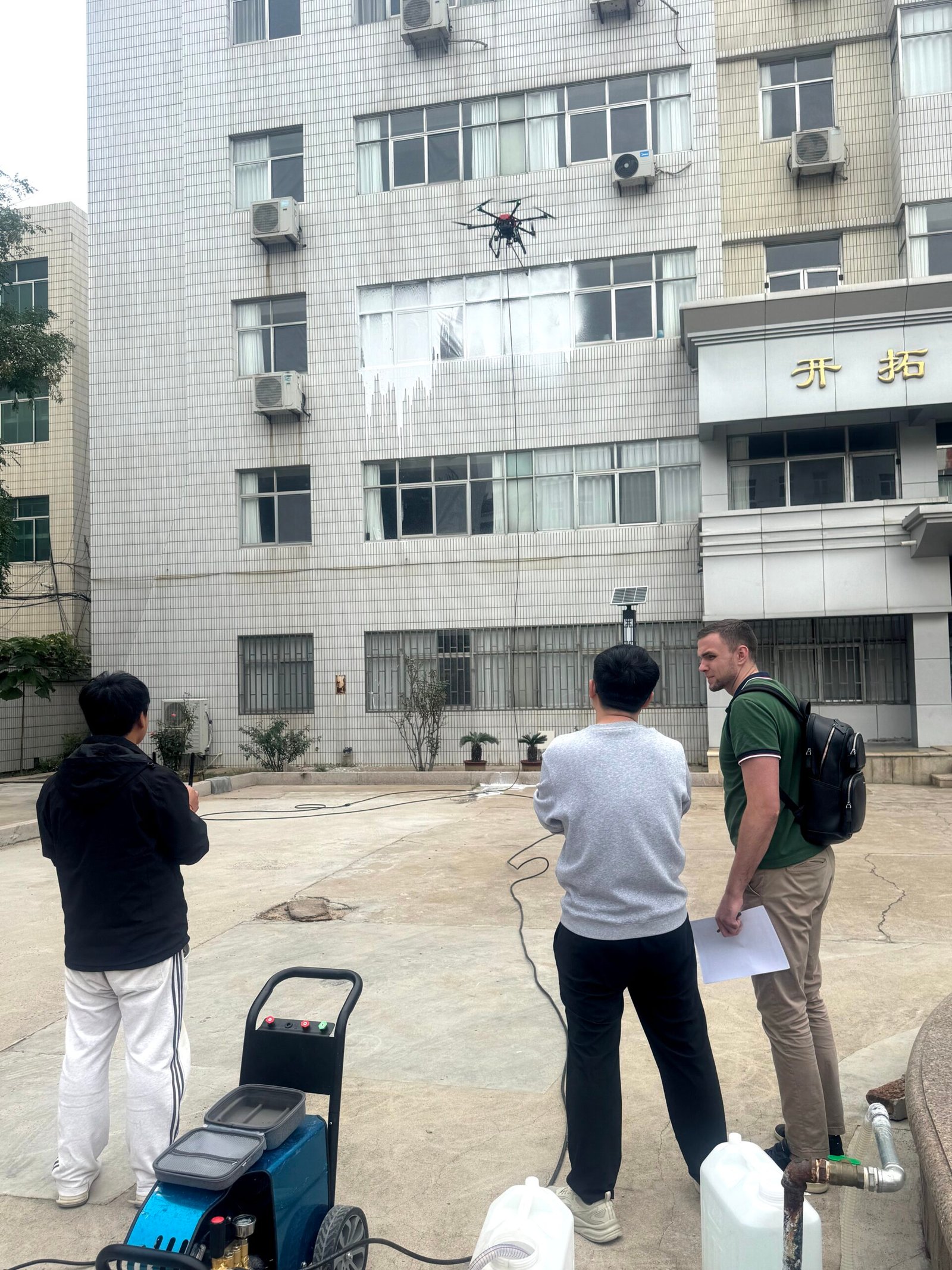 A high-pressure window cleaning drone in operation during a live demonstration for an international client at the Hoch manufacturing facility. In the foreground is the automated pump unit.
